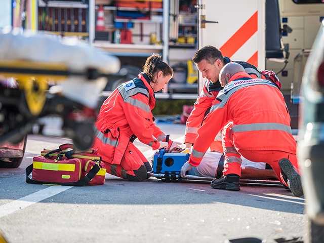 three paramedics kneeling on ground next to injured person on a stretcher