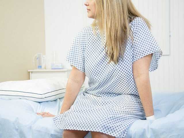 woman in white and blue hospital gown sitting on exam table in a doctor's office