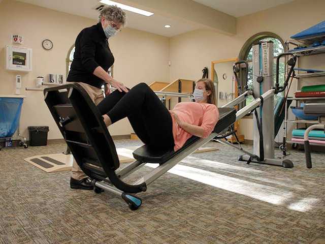 Healthcare provider assisting woman on leg press.