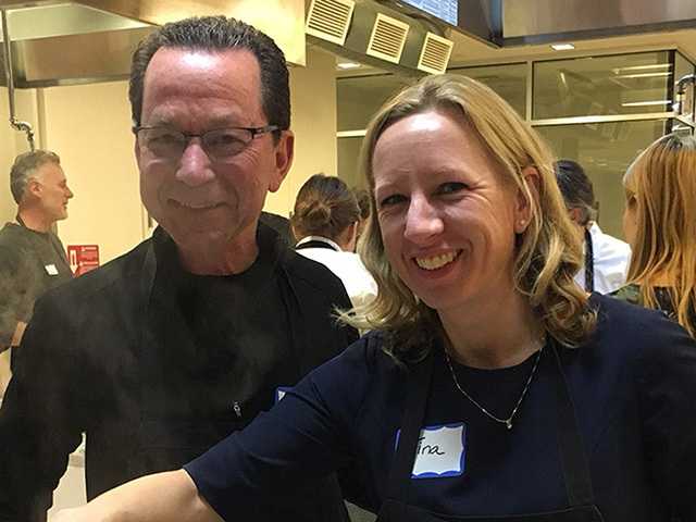 Man and woman in kitchen, smiling for photograph.