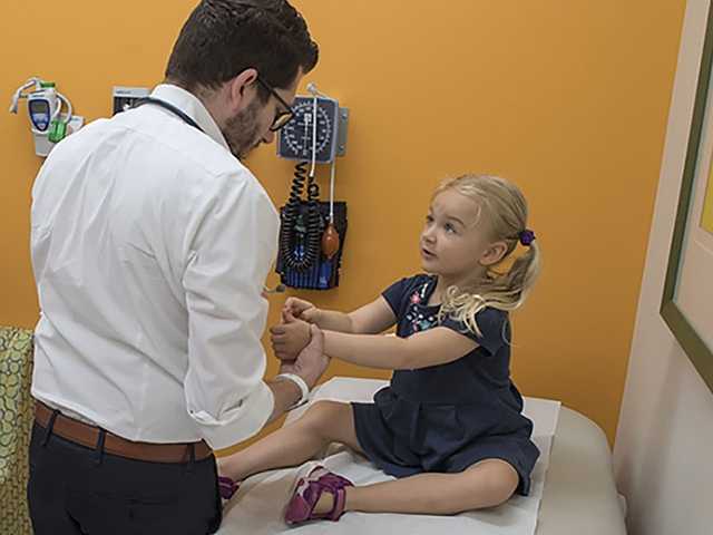 Parents watching young daughter get examined by physician.