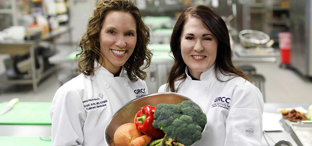 Two female chefs holding a bowl of vegetables and smiling for the photograph.