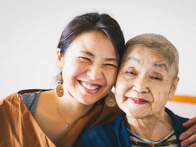 Smiling brown-haired young woman with her arm around a smiling short-haired elderly woman