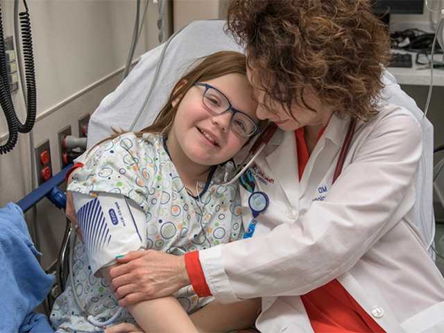 Doctor holding a child while she wears a blood pressure monitor