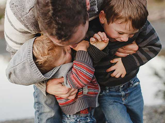 Man leaning over, hugging two young children.