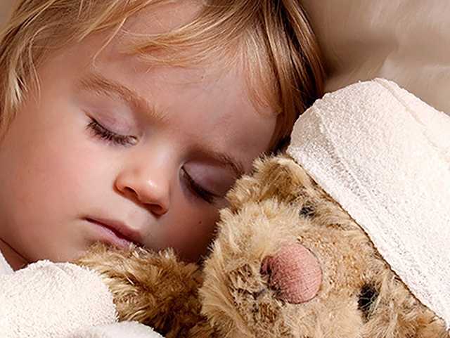 Sleeping child holding teddy bear with bandaged head.