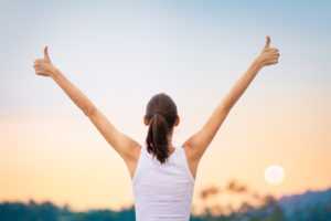 Woman with thumbs up, arms up in the air.
