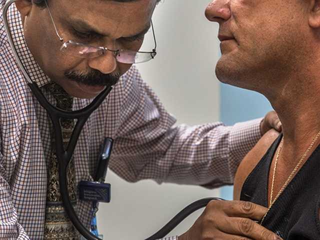 Male healthcare provider listening to mans chest with stethoscope.
