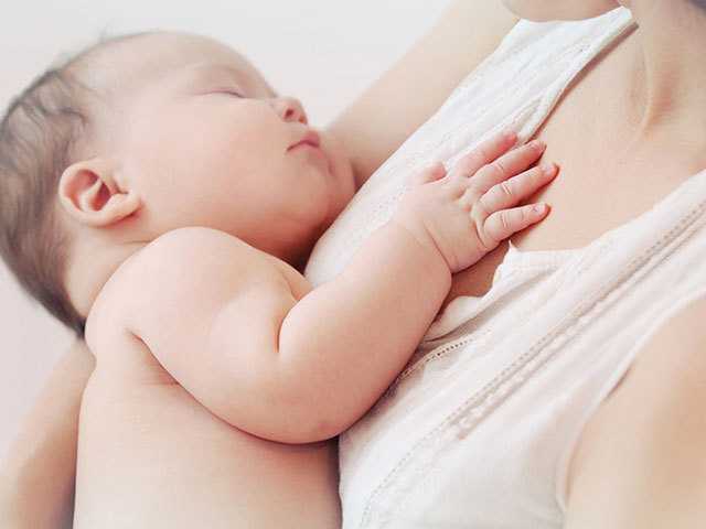 small baby with brown hair laying on mother's chese