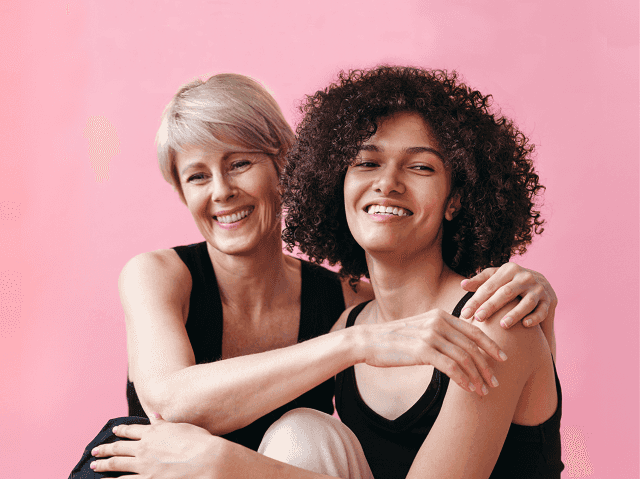 Two women hugging against pink background.