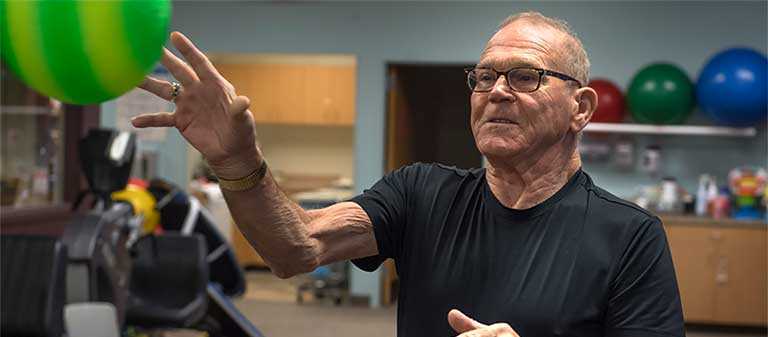 An older man in a black t-shirt is reaching for green ball