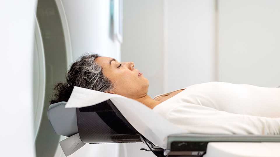 woman with dark hair lying down with closed eyes at edge of mri machine