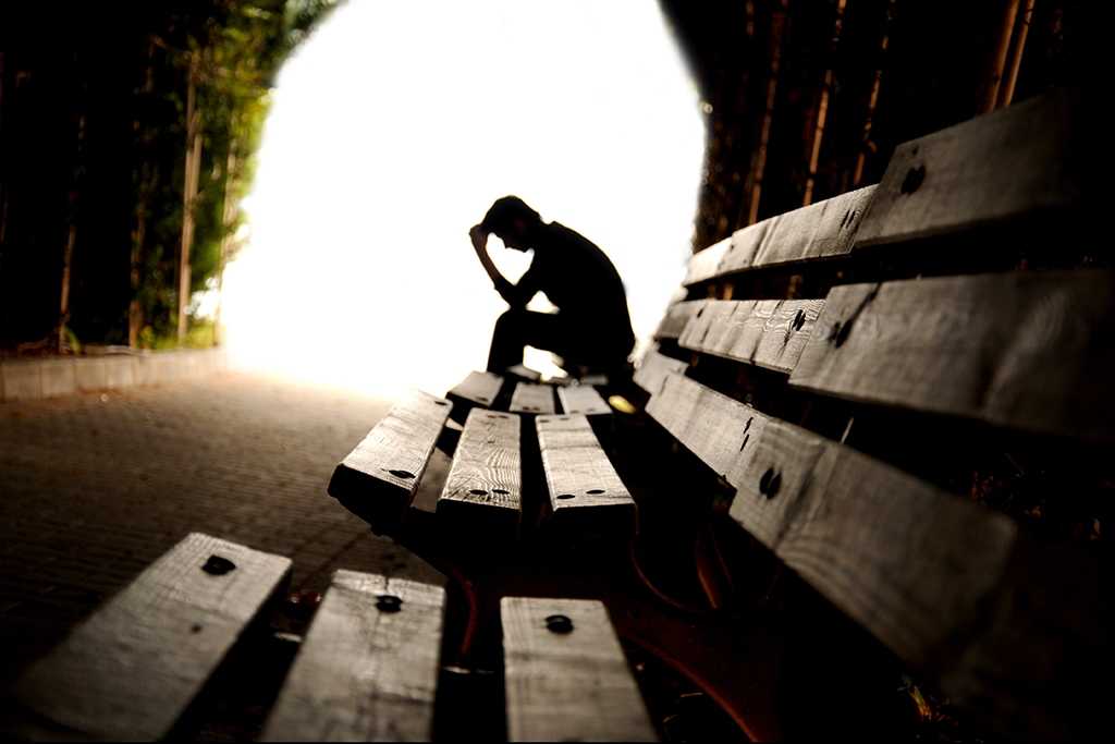 Man sitting on a bench with head in hand.