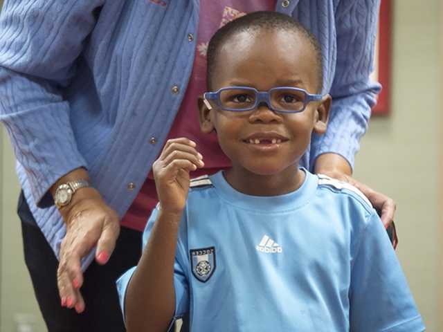Little boy with glasses and caregiver behind him